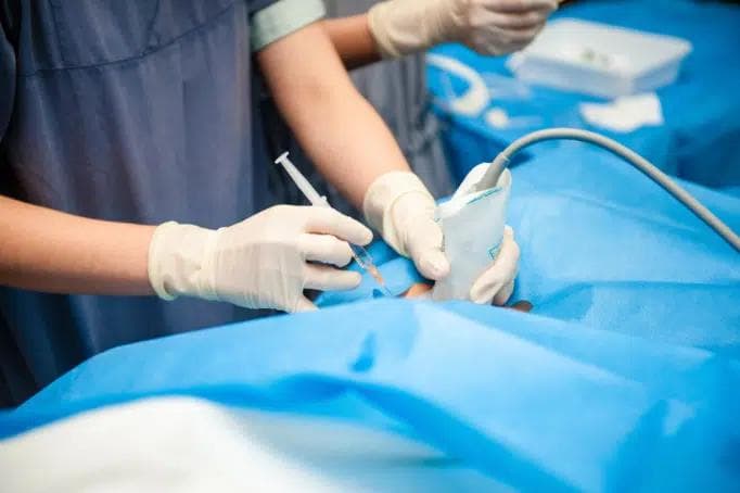 A doctor holding a syringe with an ultrasound probe guiding in for treatment.