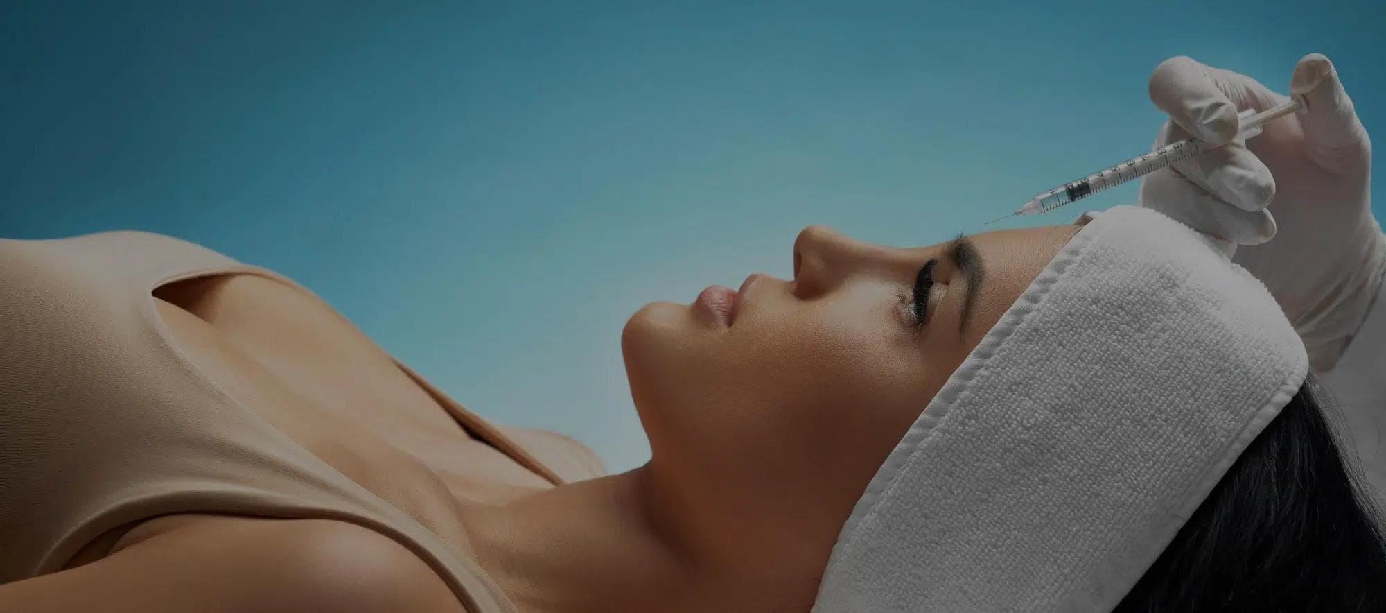 A lady that is lying supine with a small injection syringe above her forehead as though she is receiving Botox.